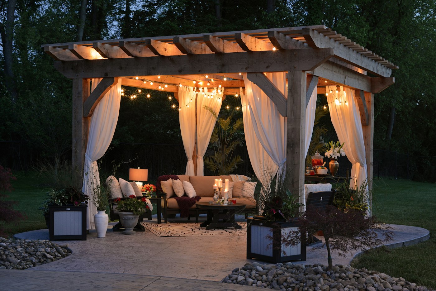 A pergola with draped curtains and warm string lights in an evening garden