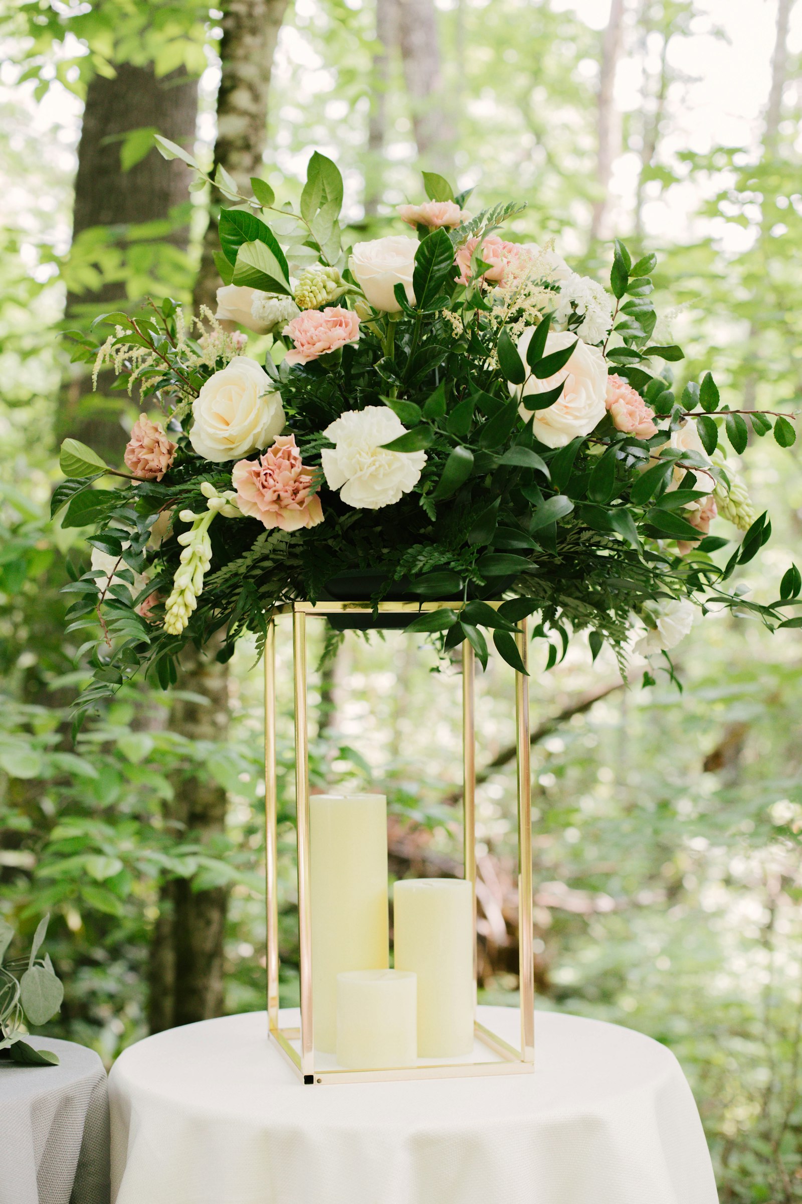 A lush arrangement of white roses and greenery on a slim gold stand
