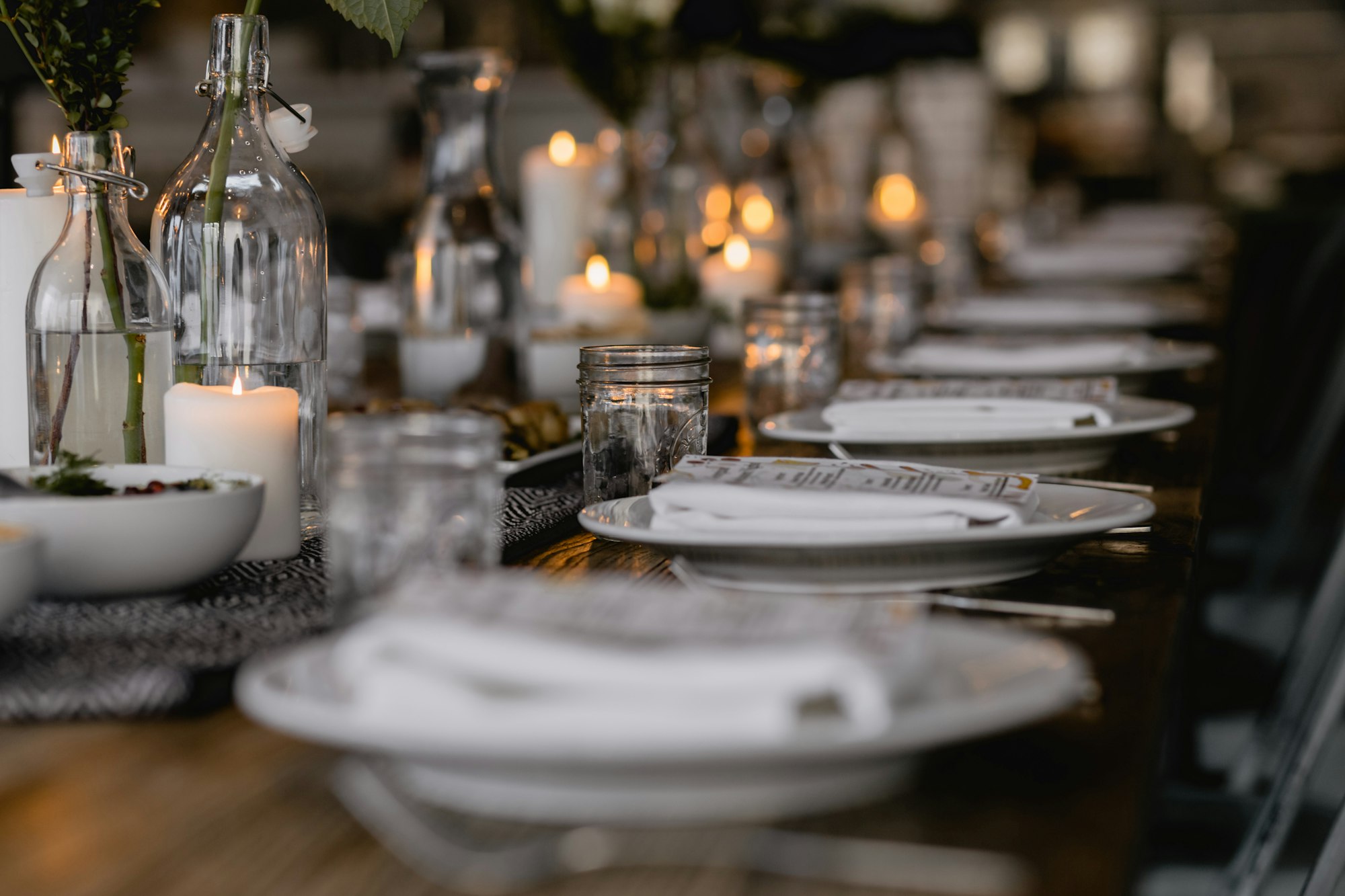 A long candlelit table set with white plates, glassware and bottles