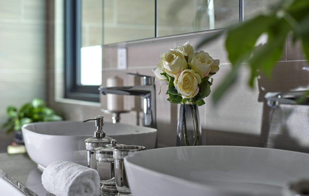 White roses in a glass vase beside a white basin in a bright restroom