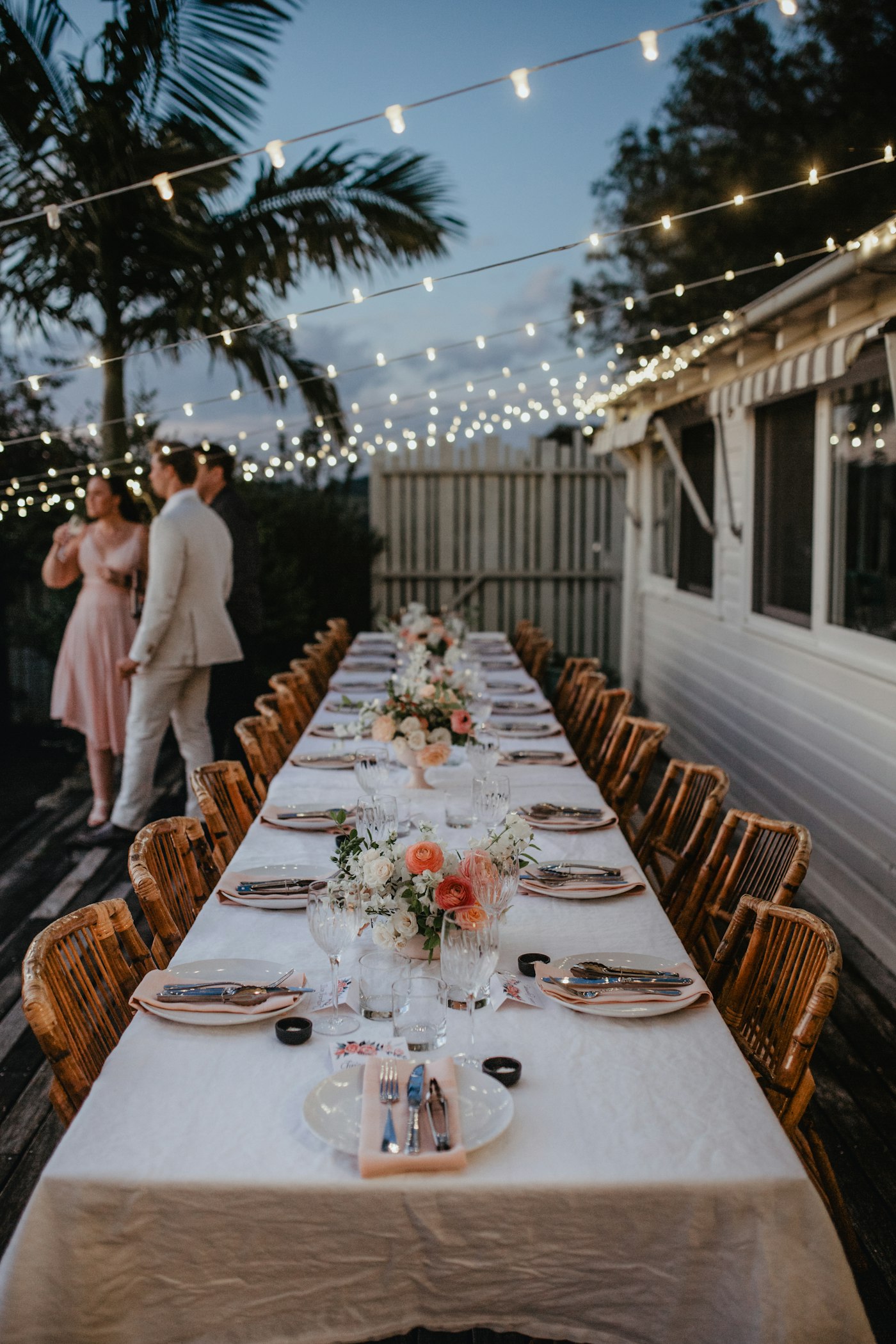 A couple standing beside a long table dressed with flowers under string lights