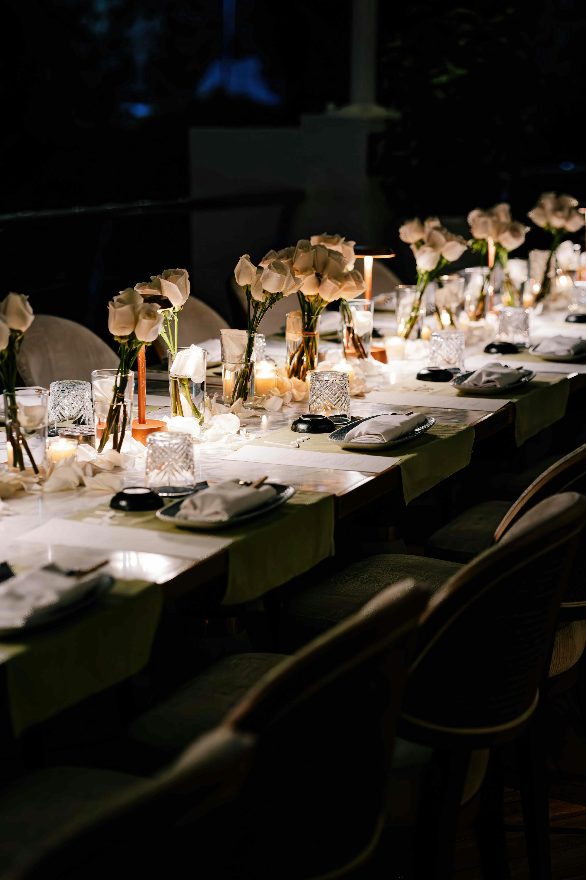 A long candlelit table dressed in deep green linens with white tulips