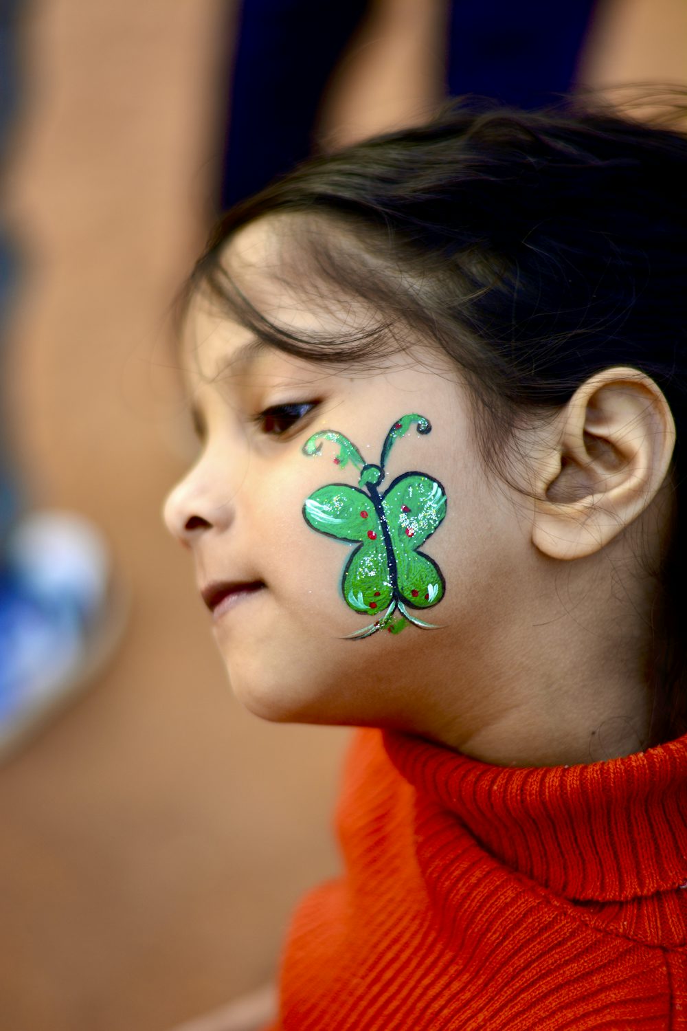 A young girl with a green butterfly painted on her cheek