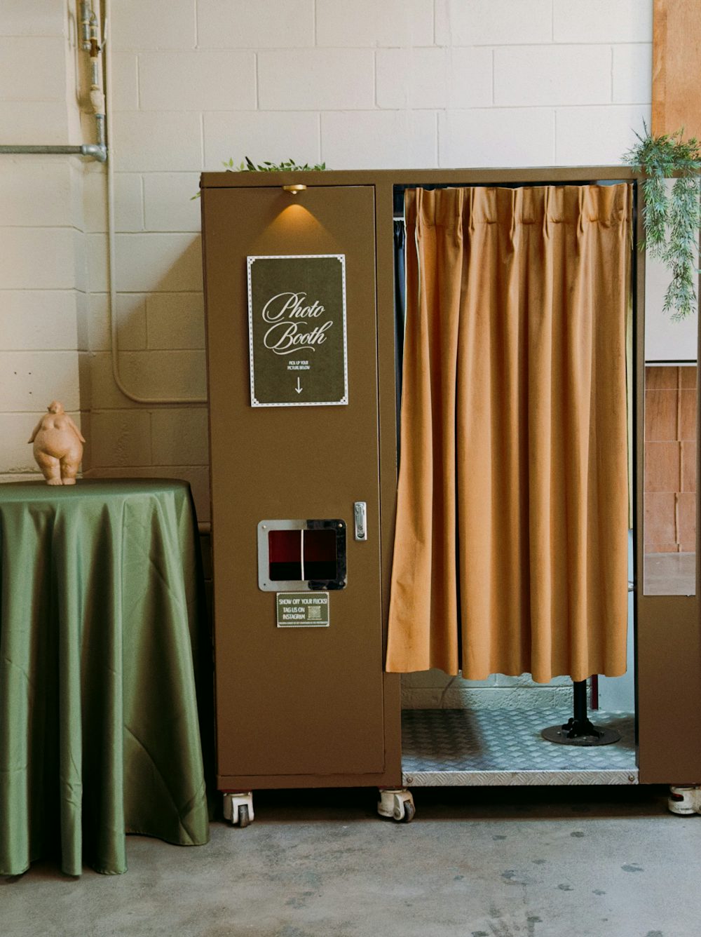A photo booth with a tan curtain beside a table dressed in olive linen