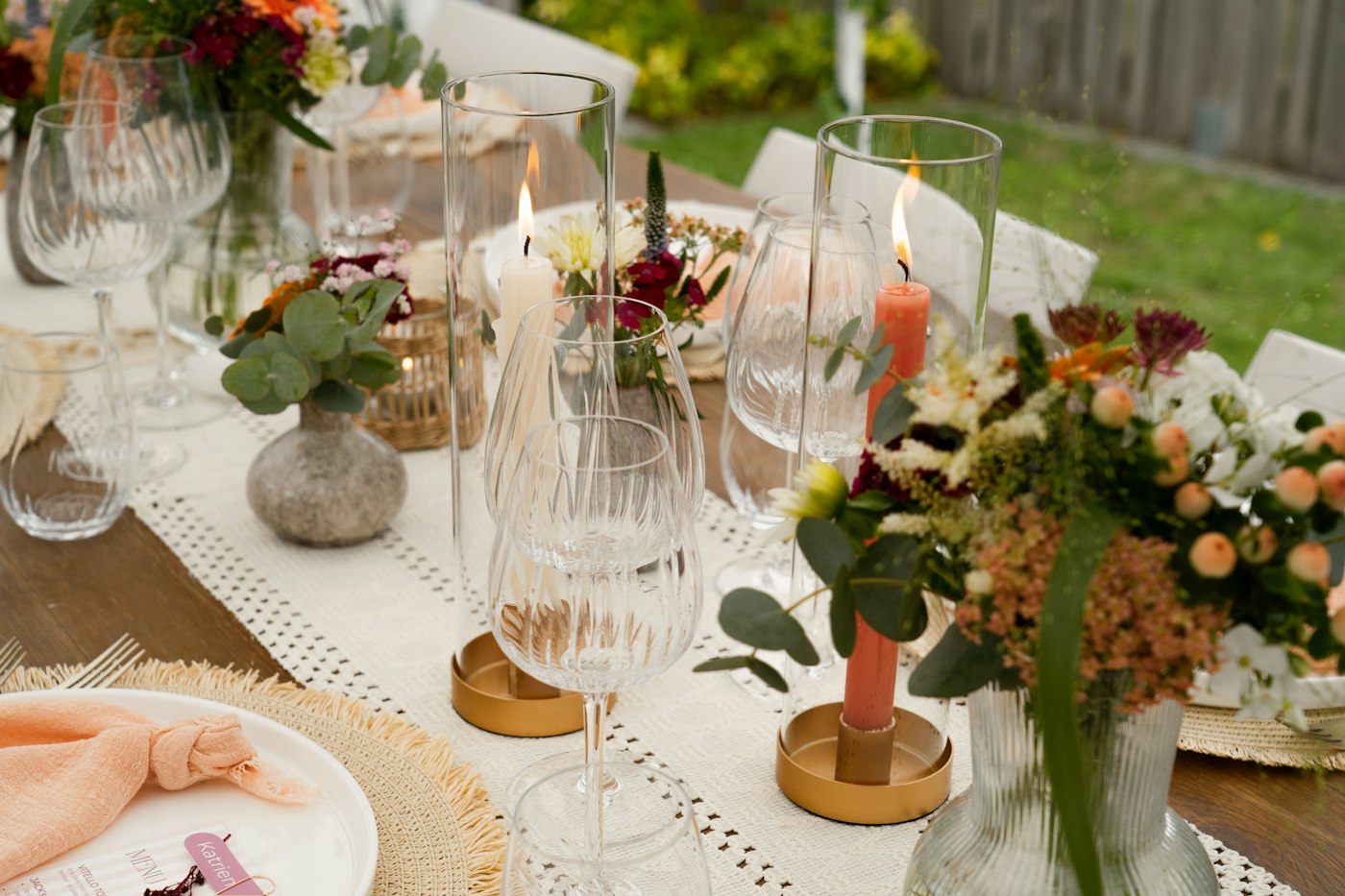 An outdoor table set with flowers, candles in brass holders and fine glassware