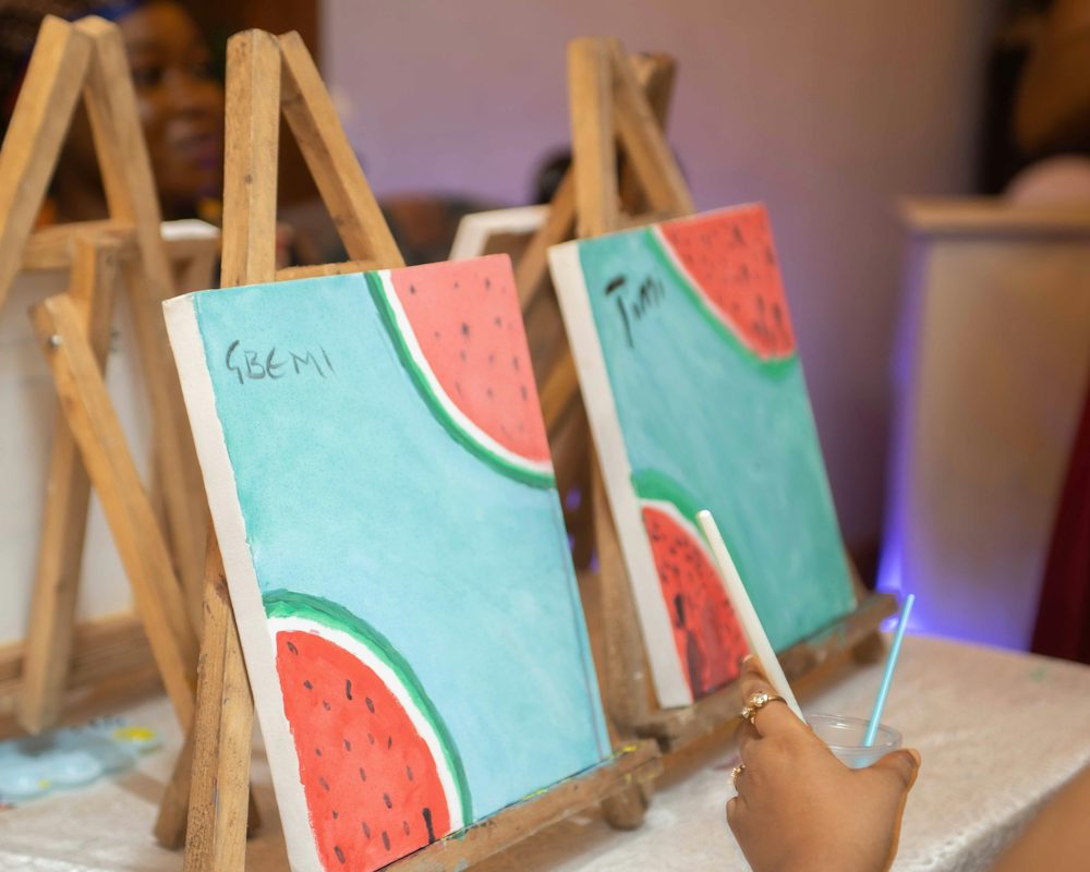 Watermelon paintings on easels with a hand holding a paintbrush