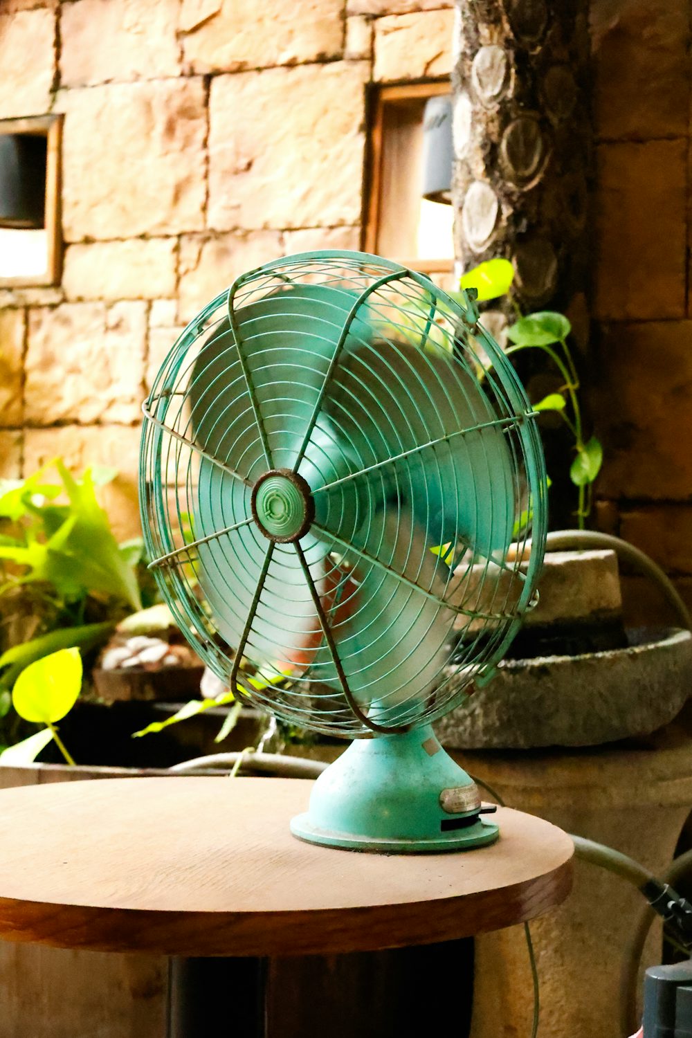 A vintage teal electric fan on a table in a garden